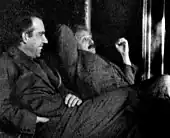 Two men sitting, looking relaxed. A dark-haired Bohr is talking while Einstein looks skeptical.