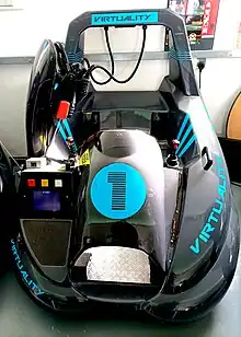 The sit-down version of the Virtuality arcade unit. The unit is a seat with two fixed position joysticks either side for game control. The headset is mounted on a hook.