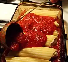 A person pouring tomato sauce over manicoti with a ladle