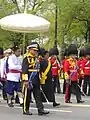 an officer carried a glòt umbrella for Princess Sirindhorn as she marched in a procession to escort the urn of Princess Bejaratna to the funeral grounds, 9 April 2012.